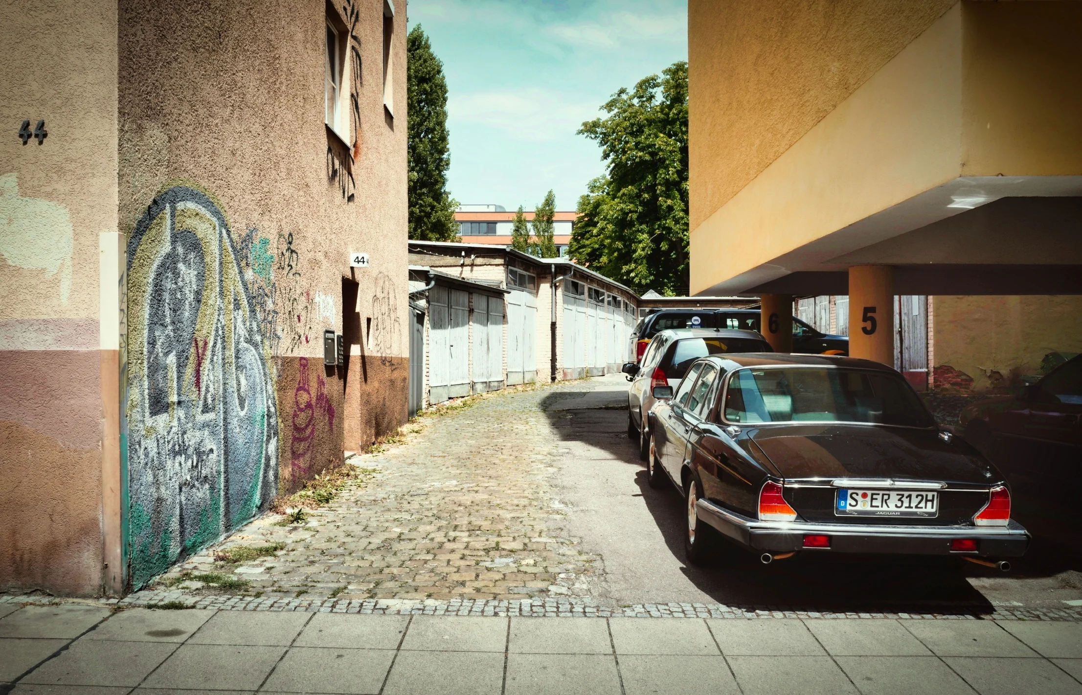 Schmaler Innenhof mit geparkten Autos und Graffiti an Wand
